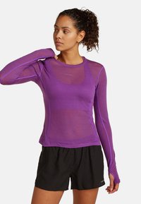 Lila Langarm-Sportoberteil, mit Netzstruktur, figurbetontem Design, Rundhalsausschnitt und kontrastierenden Nähten. Kombiniert mit schwarzen Sportshorts.