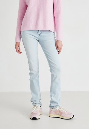Jeans de un azul claro con corte ajustado, combinados con un suéter de punto ribeteado rosa y zapatillas rosa. El suéter tiene una silueta relajada; los jeans presentan un diseño clásico.