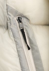 Gros plan d'une tirette de fermeture éclair noire sur un tissu à carreaux beige clair et gris avec une surface texturée et rembourrée.