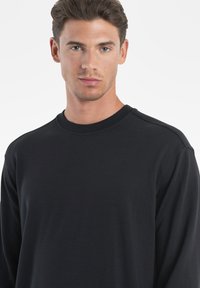 Schwarzer Langarm-Pullover mit Rundhalsausschnitt aus weichem Stoff, ausgestattet mit einem gerippten Kragen und einfachem Design. Keine sichtbaren Muster oder Akzente.