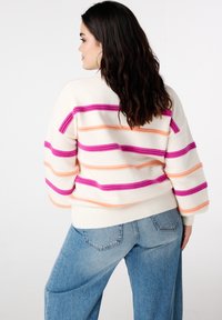 Pull en maille crème avec des rayures audacieuses rose, orange et violette. Présente une coupe décontractée et un ourlet côtelé. Porté avec un jean bleu taille haute.
