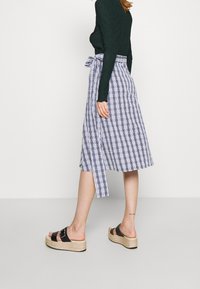 Vit och blå rutmönstrad midikjol med sidoknytning, tillsammans med svarta plattformssandaler med spänne. Ulltröja med lång ärm.