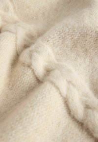 Béžová pletená tkanina s jemnou textúrou, so zapleteným vzorom a rôznymi detailmi stehov, ktoré vyjadrujú teplo a hĺbku.