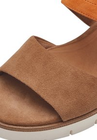Sandalo in suede marrone con una fascia arancione, caratterizzato da un ampio sottopiede e una suola in piattaforma bianca. Texture liscia e design minimalista.