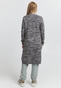 Stickad lång grå cardigan med ett texturerat mönster, ribbade manschetter och en lös passform, ihopparad med ljusgröna joggers och sneakers.