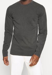 Mörkgrå bomullströja med långa ärmar och rundad hals, med subtil textur och kontrasterande sömmar; bärs med off-white byxor.