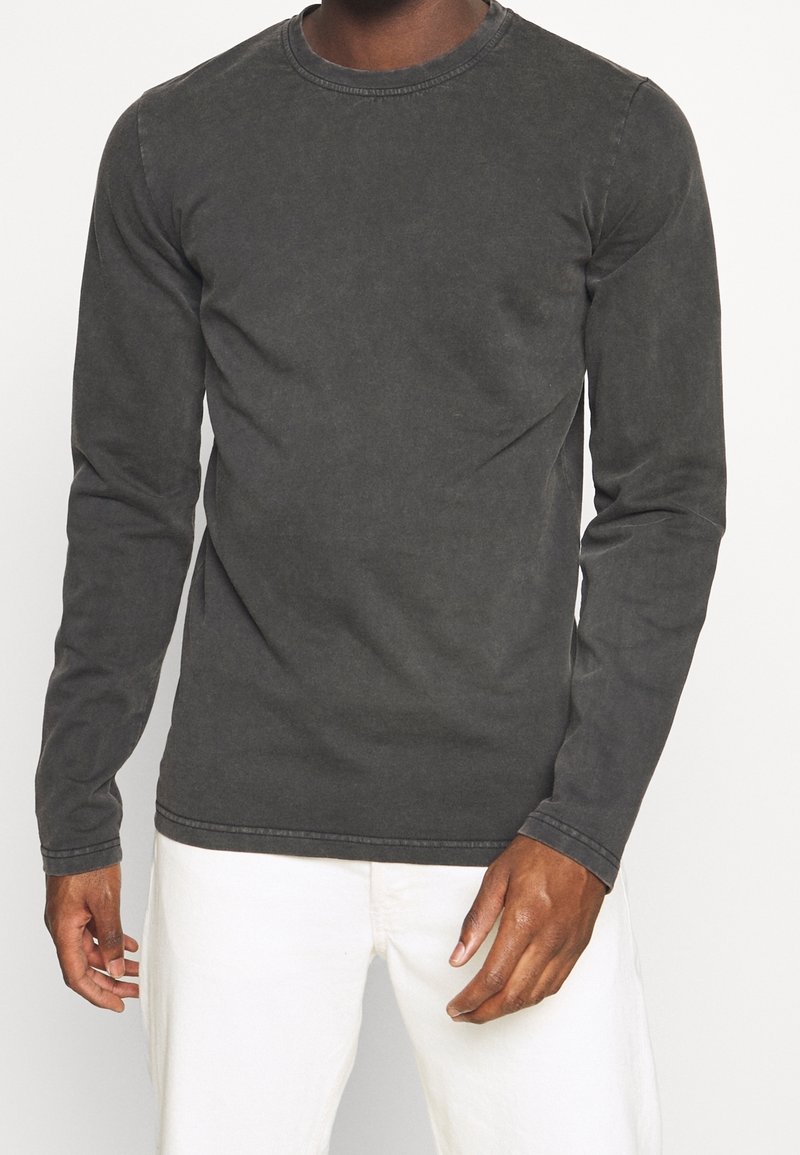 Mörkgrå bomullströja med långa ärmar och rundad hals, med subtil textur och kontrasterande sömmar; bärs med off-white byxor.