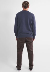 Pull marin en maille avec un ourlet côtelé porté sur un pantalon marron. Le pull présente un col rond classique et une coupe décontractée.