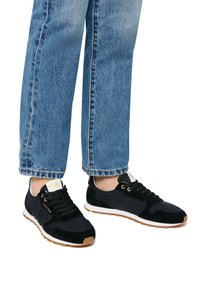 Sneaker athletic neri con un mix di texture lisce e in camoscio, design con lacci e suola in gomma color gomma. Indossati con jeans denim azzurri chiari.