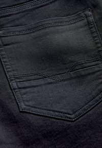 Primer plano de un bolsillo trasero de vaquero de denim gris oscuro con costuras visibles y textura de tela.