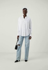 Hvit skjorte med en avslappet passform, kombinert med lyseblå ripped jeans og svarte spisse sko. Komplementerer en liten svart håndveske.