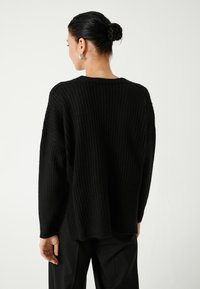 Musta ribbed neulepaita rentoa fit'iä, leveitä hihoja ja pyöreää kaula-aukkoa. Teksturoidusta neuloksesta tulee syvyyttä. Yksinkertaiset mustat housut.