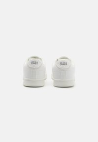 Vita låga sneakers med en slät syntetisk textur, utrustade med en vadderad krage och präglad logotyp på hälen. Minimalistisk design, gummisula.