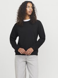 Zwarte sweatshirt met lange mouwen, geribbelde manchetten en zoom, met een ronde hals. Combinatie met lichtgrijze jeans. Eenvoudig ontwerp en textuur.