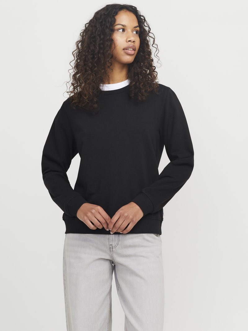 Zwarte sweatshirt met lange mouwen, geribbelde manchetten en zoom, met een ronde hals. Combinatie met lichtgrijze jeans. Eenvoudig ontwerp en textuur.