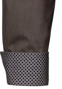 Manica in tessuto rigato marrone con un polsino a motivo geometrico bianco, che presenta uno sfondo blu navy e piccoli quadrati.