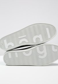 Semelles de chaussures en caoutchouc blanc avec texture côtelée, nom de la marque "hægli" imprimé en gris clair. Bords lisses et design minimaliste.