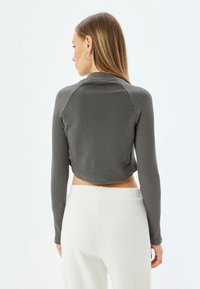 Gray cropped sweater with ribbed texture, long sleeves, round neckline, and contrasting fabric on the shoulders, worn with white pants.