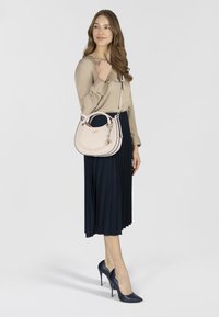 Blusa beige, gonna plissettata blu navy e scarpe con tacco blu navy. La borsa è rosa chiaro con texture perforata e un charm rimovibile.