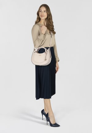 Beige blouse, marineblauwe geplooide rok en marineblauwe hoge hakken. De tas is lichtroze met een geperforeerde textuur en een afneembare charm.