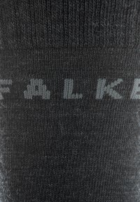 Sort strikket sok med ordet "FALKE" i en lysere nuance, som viser en glat tekstur og sømfri design.