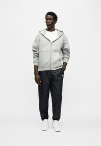 Γκρι φούτερ με φερμουάρ και τσέπες καγκουρό, συνδυασμένο με μαύρο στενό παντελόνι jogging και λευκά αθλητικά παπούτσια. Απλή, καθημερινή αθλητική ενδυμασία.