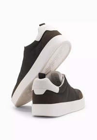 Bruna lädersneakers med en vit detalj vid hälen, tjock vit gummisula och en strukturerad bakpanel. Enkelt, modernt design med dragflik.