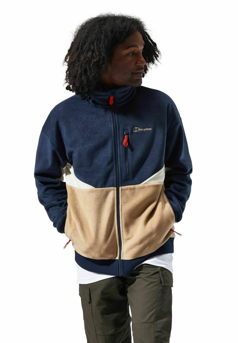 Marineblaues Fleece-Jacke mit cremefarbenen und sandfarbenen Einsätzen, hohem Kragen und roten Reißverschluss-Zügen. Sie verfügt über Seitentaschen und ein Logo auf der Brust.