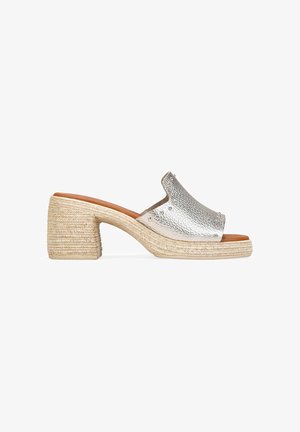 Mule de cuero plateado con puntera abierta, tacón de bloque envuelto en yute y detalle de tachuelas metálicas en la parte superior.