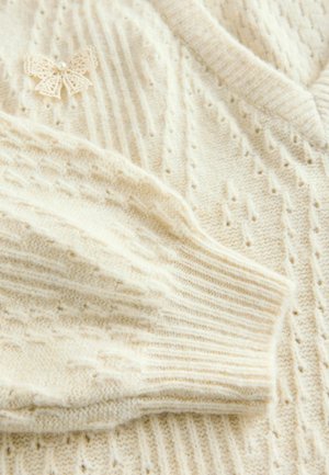 Crème gebreide sweater met een geribde kraag en mouwboorden, voorzien van een textuurdesign en een delicate strikaccent met kantpatroon.