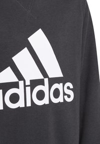 Sudadera de color gris oscuro con un gran logo blanco de Adidas en el pecho y tres franjas diagonales. Textura suave, diseño de cuello redondo.