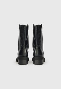 Botine negre din piele, cu o textură netedă, detalii cu fermoar la spate și un toc jos și gros. Design simplu și funcțional.