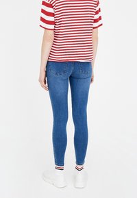Jeans ajustados de mezclilla en azul medio, combinados con una camiseta de manga corta a rayas rojas y blancas. Presenta un diseño ajustado y zapatillas blancas.
