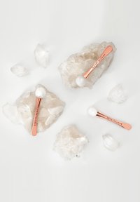 Strumenti per il viso in oro rosa con teste di cristallo bianco lucido poggiati su cristalli di quarzo traslucido grezzo, evidenziando il contrasto tra texture e colore.