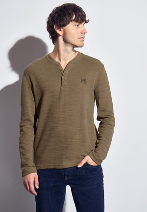 Maglietta henley a maniche lunghe verde oliva con tre bottoni, tessuto texturizzato, orlo tondo e un piccolo logo sul lato sinistro del petto.