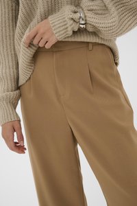 Pull en tricot beige avec des poignets côtelés, associé à un pantalon structuré brun clair comportant des poches latérales et une texture lisse.
