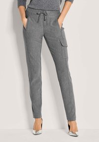 Vrouw in aansluitende grijze cargobroek met een trekkoord in de taille en zijzakken, gecombineerd met glanzende zilveren puntige hakken.