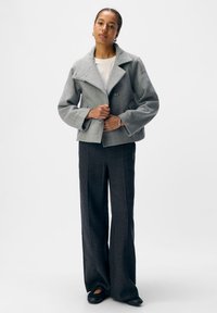 Graue, kurz geschnittene Jacke mit weitem Kragen und Knöpfen, kombiniert mit dunkelblauen, weit geschnittenen Hosen. Der Stoff hat eine weiche Textur und ein dezentes Muster.