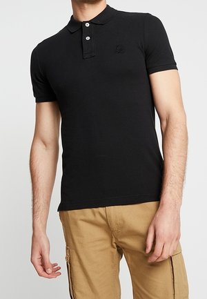 Schwarzes Polohemd mit Kragen, kurzen Ärmeln, einer Drei-Knopf-Leiste und einem kleinen Logo auf der Brust. Modell trägt helle Khakihosen.