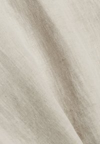 Tissu en lin beige naturel avec une texture de tissage visible et de douces plis créant des ombres et des reflets délicats.