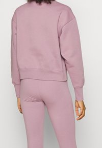 Felpa viola chiaro con scollo tondo e polsini a costine, abbinata a leggings coordinati. Il tessuto appare morbido e testurizzato.