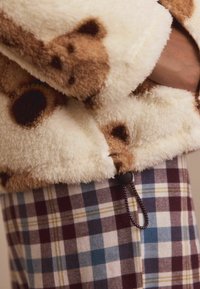 Brązowa, plamista dzianina z miękką teksturą współgra z wielokolorowym wzorem w kratkę w odcieniach niebieskiego, burgundowego i kremowego.