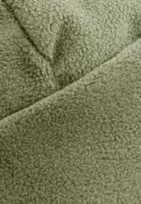 Texturerad grön fleece tyg med en mjuk, fluffig yta, i en dämpad olivnyans med svaga tonvariationer.