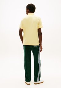 Κίτρινο πόλο πουκάμισο και πράσινο παντελόνι βελουτέ με λευκές πλαϊνές ρίγες. Κανονική εφαρμογή, μονόχρωμο, εμφανείς ραφές και casual σχεδιασμός.