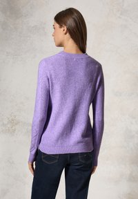 Pull violet en maille côtelée avec des manches longues, un col rond et une coupe légèrement ajustée, associé à un pantalon en denim foncé.