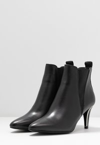 Svarta läderankelstövlar med spetsig tå och smal klack. Har elastiska sidor, en slät yta och metalliska detaljer på klacken.