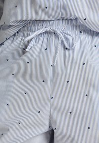 Ριγέ πυτζάμα σορτς με κορδόνι στη μέση, κατασκευασμένα από ελαφρύ ύφασμα με ναυτικά μπλε καρδιές διάσπαρτες σε λευκό φόντο.