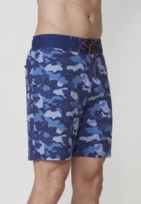 Modré plavky s geometrickým camouflage vzorom, s nastaviteľným pásom a bočnými vreckami. Materiál je ľahký a rýchloschnúci.