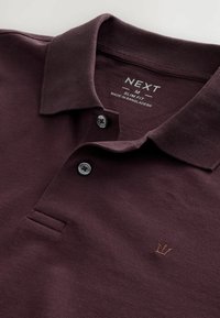 Burgundská polo košeľa s textúrovanou tkaninou, úzky strih, pätica s tromi gombíkmi a malým vyšitým logom na hrudi.