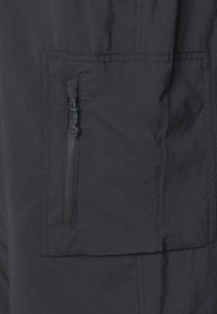 Tmavošedá látka s hladkou textúrou obsahuje zipsový vrecko a ploché nášivkové vrecko, ktoré sú precízne prešité s minimálne viditeľnými švami.